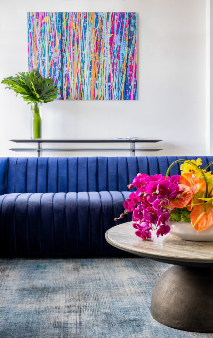 A living room with blue couch and colorful flowers.